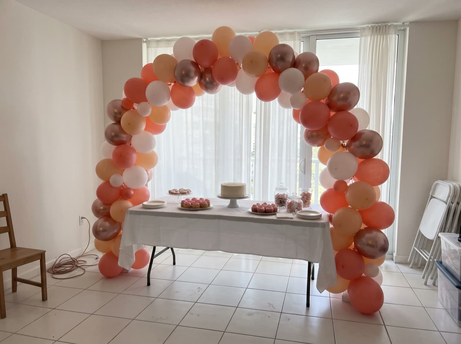 Organic balloon arch in coral, peach and white over a dessert table in a Miami condo